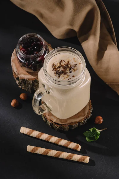 Vista close-up de vidro com milkshake em fatia de madeira, groselhas, nozes, hortelã, palhas doces e toalha de cozinha — Fotografia de Stock