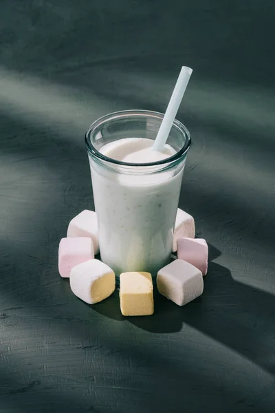 Closeup view of milkshake glass with drinking straw and marshmallows on table — Stock Photo