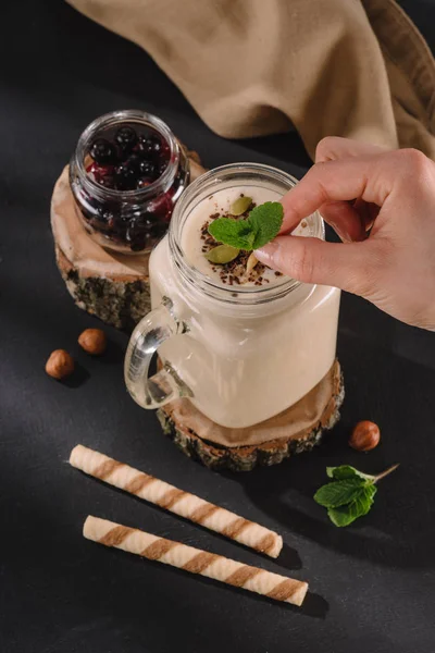 Cropped shot of female hand putting mint in milkshake, sweet straws, walnuts and currants — Stock Photo