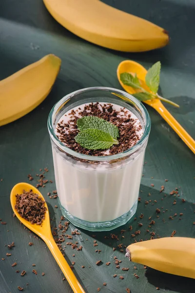 Closeup shot of milkshake with mint leaves and chocolate shavings, spoons and bananas — Stock Photo