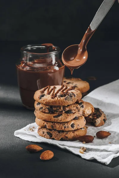 Primer plano de chocolate líquido vertiendo en galletas apiladas de chispas de chocolate - foto de stock