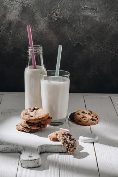 Chocolate-chip cookies on white wooden cutting board with milk — Stock Photo