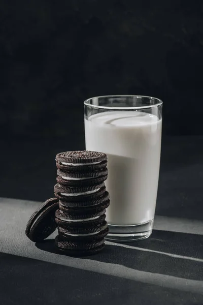Delicious sandwich cookies with glass of milk on black surface — Stock Photo