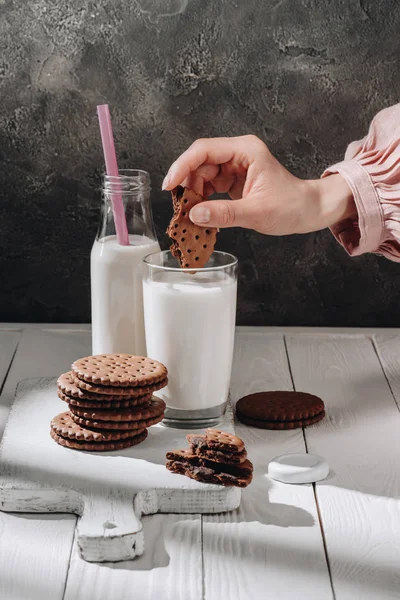 Foto recortada de la mujer sumergiendo deliciosa galleta en un vaso de leche - foto de stock