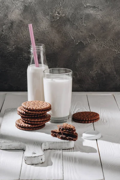 Стопка вкусного печенья со стеклом и бутылкой молока на белом деревянном столе — стоковое фото