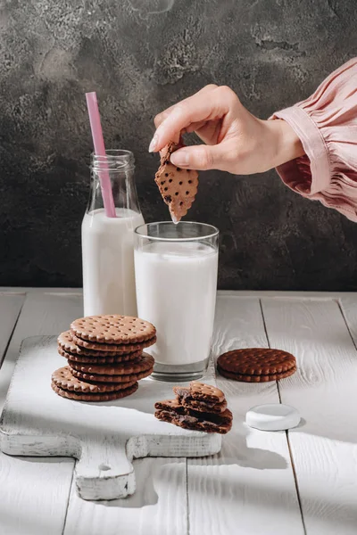 Cropped shot of woman dipping chocolate cookie into glass of milk — Stock Photo
