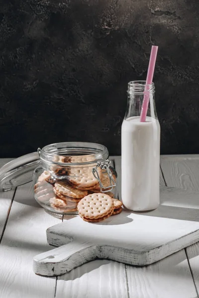 Delicious cookies in glass jar with bottle of milk — Stock Photo