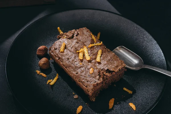 Nahaufnahme von Schokoladenkuchen mit Orangenschale auf schwarzem Teller — Stockfoto