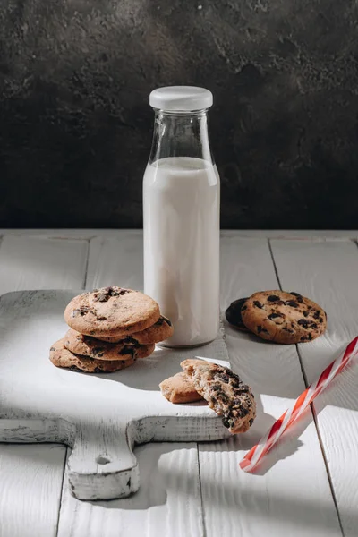 Deliciosos biscoitos de chocolate com garrafa de leite em tábua de madeira — Fotografia de Stock