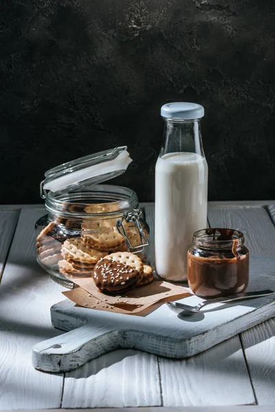 Delicious cookies dipped in hot chocolate and sesame with bottle of milk — Stock Photo