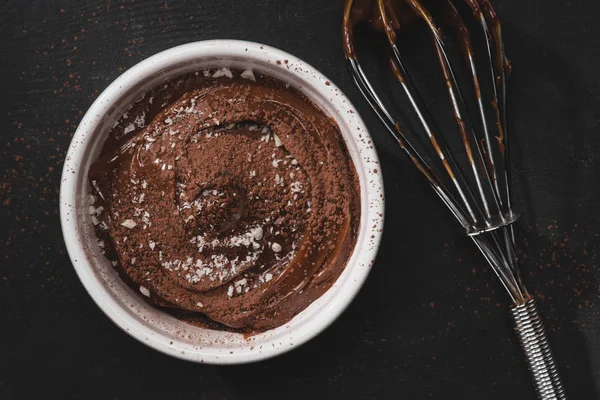 Top view of bowl with chocolate pudding and whisk on black table — Stock Photo
