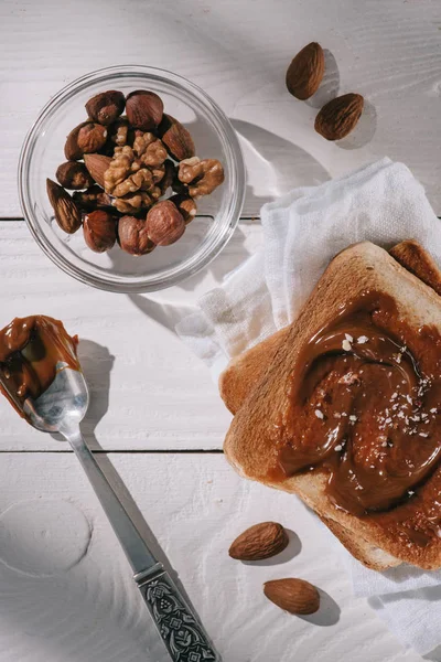 Top view of toast bread with chocolate and different nuts in bowl on white wooden table — Stock Photo