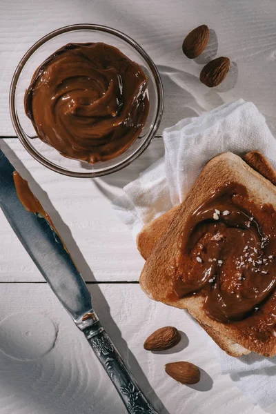 Pan tostado con chocolate y cuchillo sobre mesa de madera blanca - foto de stock