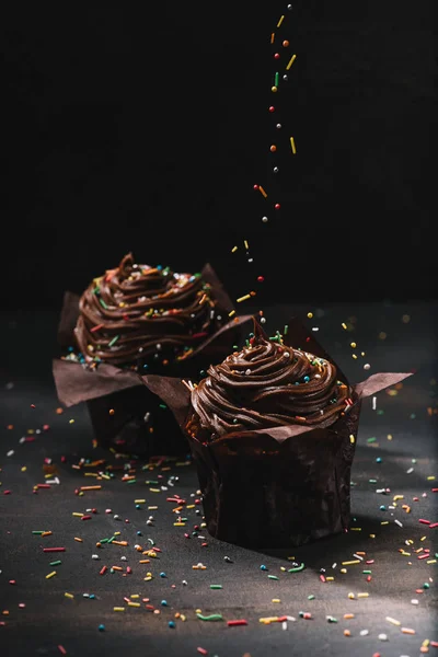 Tasty chocolate cupcakes with cream and sugar spreading on table — Stock Photo