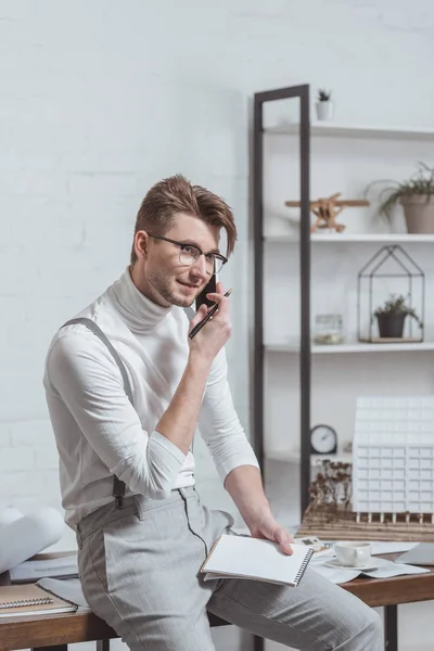 Architektenporträt mit Brille und Notizbuch im Gespräch auf dem Smartphone am Arbeitsplatz im Büro — Stockfoto