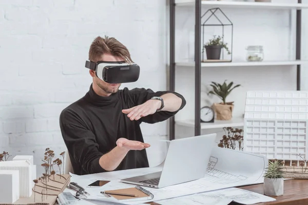 Architect in vr headset at workplace with laptop, schemes and building models in office — стоковое фото