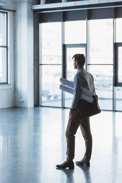 Side view of architect with blueprints in bag standing in empty building — Stock Photo