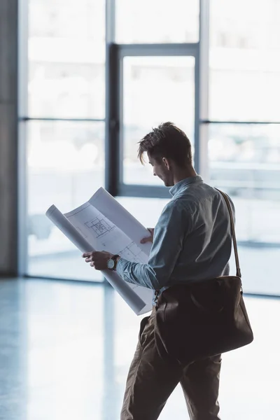 Side view of architect looking at blueprint in hands in empty building — Stock Photo