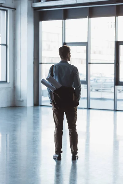 Back view of architect with bag full of blueprints standing in empty building — Stock Photo