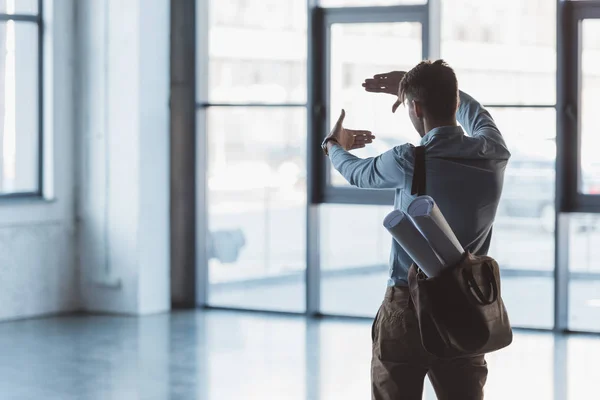 Back view of architect with bag full of blueprints measuring empty building — Stock Photo