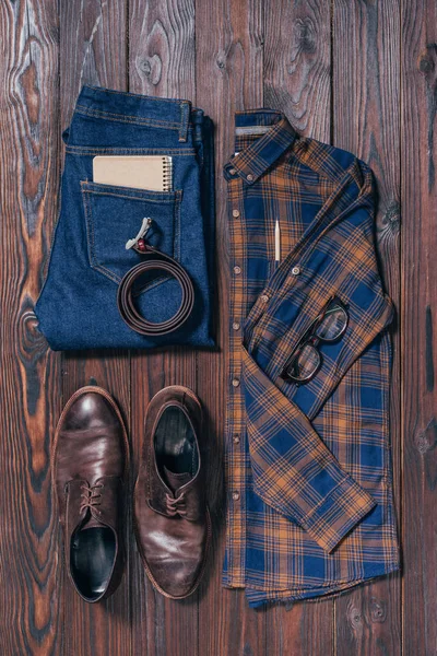 Posa piatta con camicia alla moda maschile, scarpe, jeans, occhiali e cintura disposti su superficie in legno — Foto stock