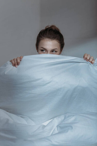 woman covering face with bedcover