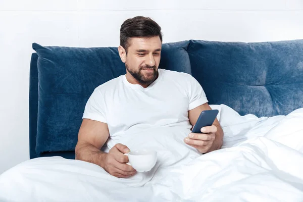Young man using smartphone in bed — Stock Photo, Image