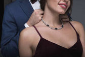 man in tuxedo putting necklace on girlfriend