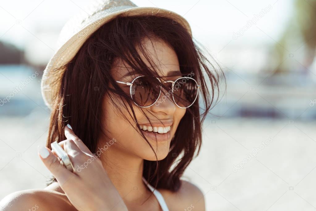 Крупный план портрет красивой брюнетки в солнечных очках и соломенной шляпе, смотрящей в сторону пляжа