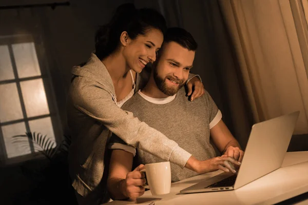Χαμογελαστά ζευγάρι χρησιμοποιώντας φορητό υπολογιστή στο σπίτι — Φωτογραφία Αρχείου