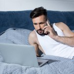 Young man using gadgets in bed