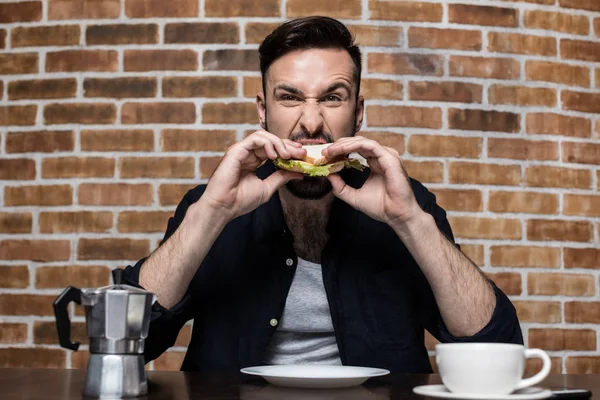 Γενειοφόρος νέος άνθρωπος τρώει σάντουιτς — Φωτογραφία Αρχείου