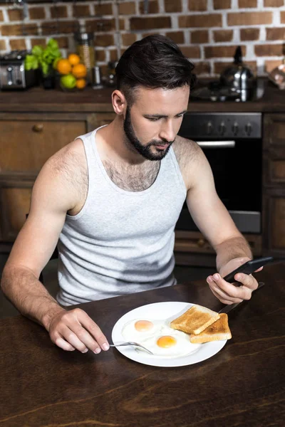 Человек с помощью смартфона во время завтрака — Бесплатное стоковое фото