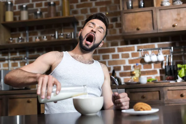 Yawning man pouring milk at breakfast — Stock Photo, Image