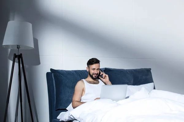 Handsome man using gadgets in bed — Free Stock Photo