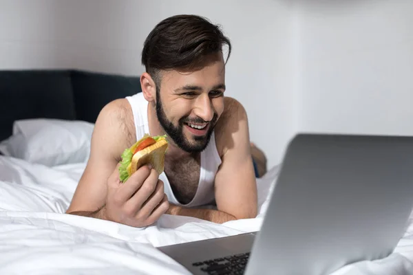 Skäggig man använder laptop i sängen — Stockfoto