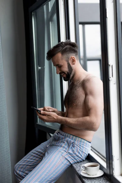 Hemdloser Mann benutzt Smartphone auf Fensterbank — Stockfoto