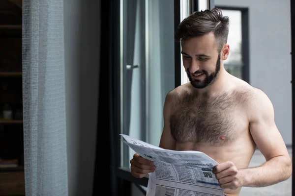 Улыбающийся мужчина без рубашки читает газету — Бесплатное стоковое фото