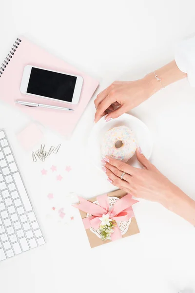 Mãos femininas com donut no local de trabalho — Fotografia de Stock