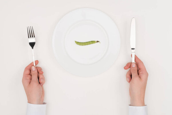 hands, cutlery and pea on plate