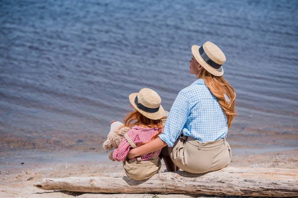 Mother and daughter with teddy bear on beach — Stock Photo, Image