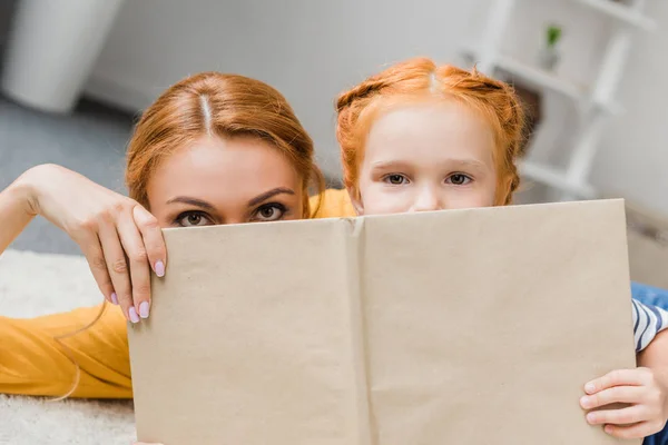 Mother and daughter hiding by book — Stock Photo, Image