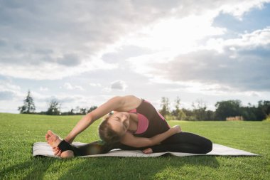 Genç kadın parkta yoga yapıyor.