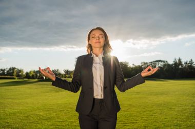 smiling businesswoman meditating in park clipart