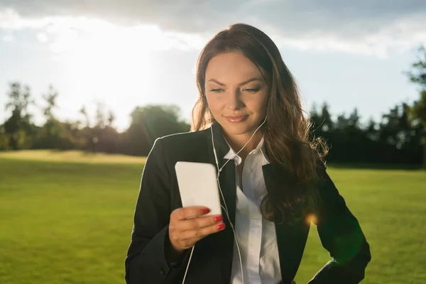 Businesswoman in earphones with smartphone — Stock Photo, Image