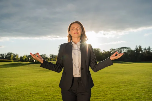 Leende affärskvinna mediterar i park — Stockfoto