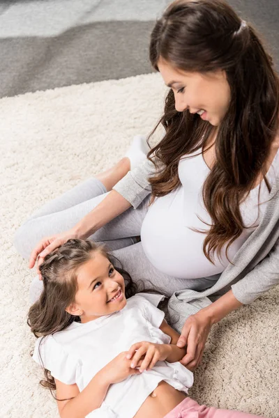 Беременная женщина с дочерью, сидящей на ковре — стоковое фото