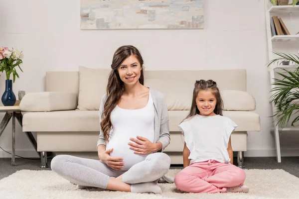 怀孕的妇女，带着女儿坐在地毯上 — 免费的图库照片