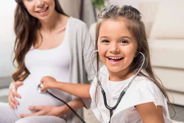 Dívka posloucháte těhotné břicho prostřednictvím stetoskop — Stock fotografie