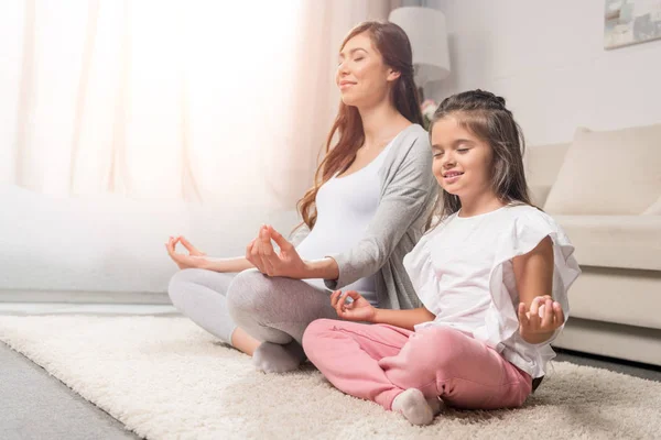 Pregnant woman with daughter in lotus pose — Stock Photo, Image